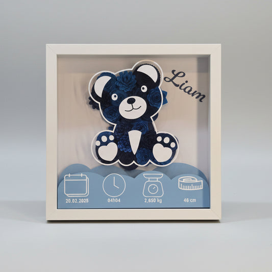 Cadre de naissance personnalisé 3D avec ours en fleurs de papier bleu. Décoration souvenir pour chambre de bébé incluant le prénom Liam, la date du 20.02.2025, l'heure de naissance (04h04), le poids (2,650 kg) et la taille (46 cm). Tableau artisanal dans un cadre blanc profond.