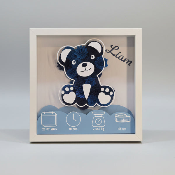 Cadre de naissance personnalisé 3D avec ours en fleurs de papier bleu. Décoration souvenir pour chambre de bébé incluant le prénom Liam, la date du 20.02.2025, l'heure de naissance (04h04), le poids (2,650 kg) et la taille (46 cm). Tableau artisanal dans un cadre blanc profond.